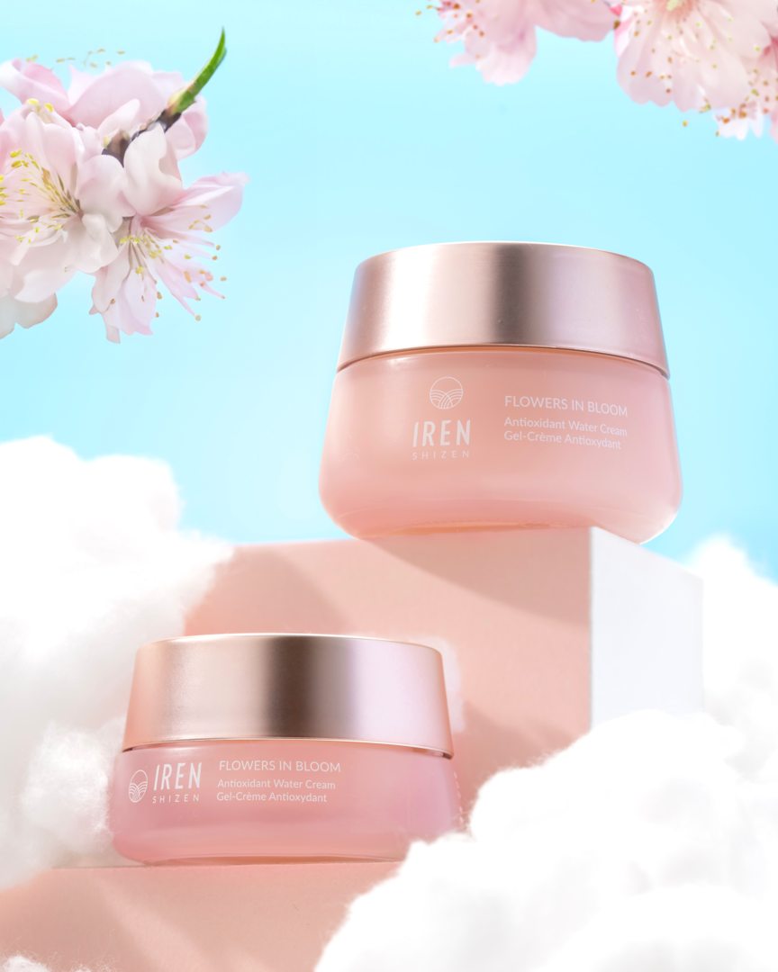 Two jars of "FLOWERS IN BLOOM" Antioxidant Water Cream by IREN Shizen are gracefully showcased on a cloud-like surface, surrounded by blooming cherry blossom branches and set against a clear blue sky. This silicone-free gel cream is ideal for sensitive skin, offering hydration without irritation. #all-groups