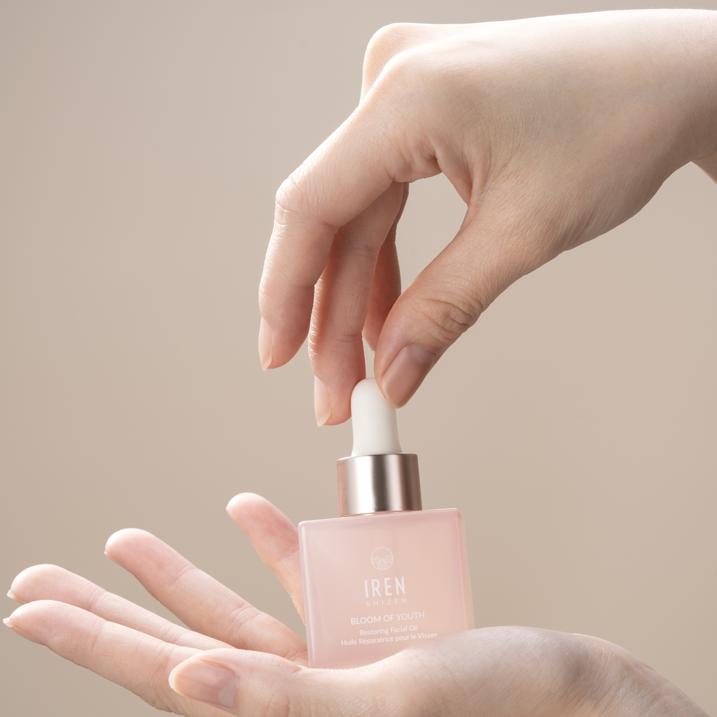 A woman's hand holding a bottle of LES ESSENTIELS Best Sellers Set from the IREN Shizen brand.