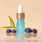 A blue dropper bottle labeled "IREN Shizen TIMELESS ELIXIR Hydrating Eye Skincare Kit" sits on a reflective surface with three blueberries and a green leaf in the background, ideal for those seeking hydration and addressing dark circles.