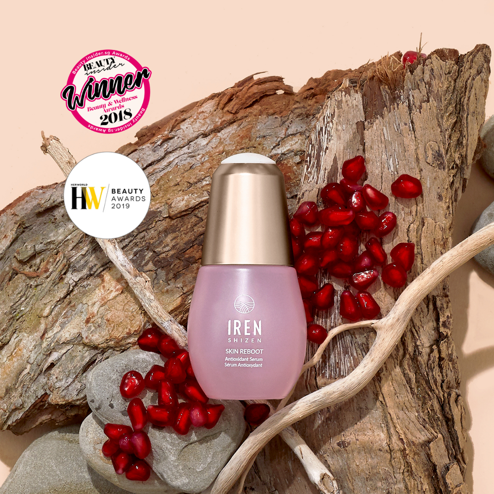 A bottle of IREN Shizen SKIN REBOOT Antioxidant Serum is shown on wood with pomegranate seeds, next to two award badges from 2018 and 2019.