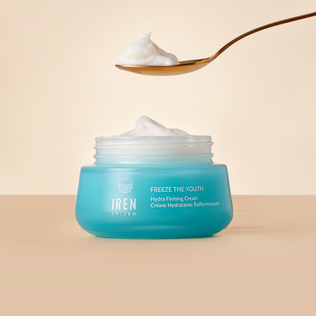 A jar of IREN Shizen 'FREEZE THE YOUTH' Hydra Firming Cream, an acne treatment with Grape Extract for sebum balance, with a dollop on a spoon above it, conveying the product's creamy texture.