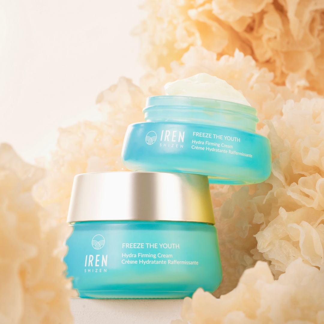 Image of two blue jars of FREEZE THE YOUTH Hydra Firming Cream by IREN Shizen with the age-defying formula, placed among light brown decorative fibers. The cream, enriched with snow mushroom extract, is visible in the top jar, which is open, while the bottom jar is closed. #all-groups