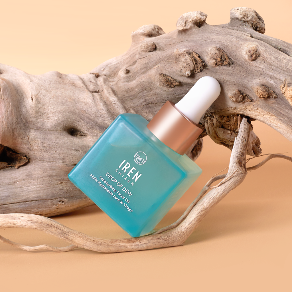 A bottle of customized DROP OF DEW Moisturizing Facial Oil by IREN Shizen, sitting on a piece of driftwood.