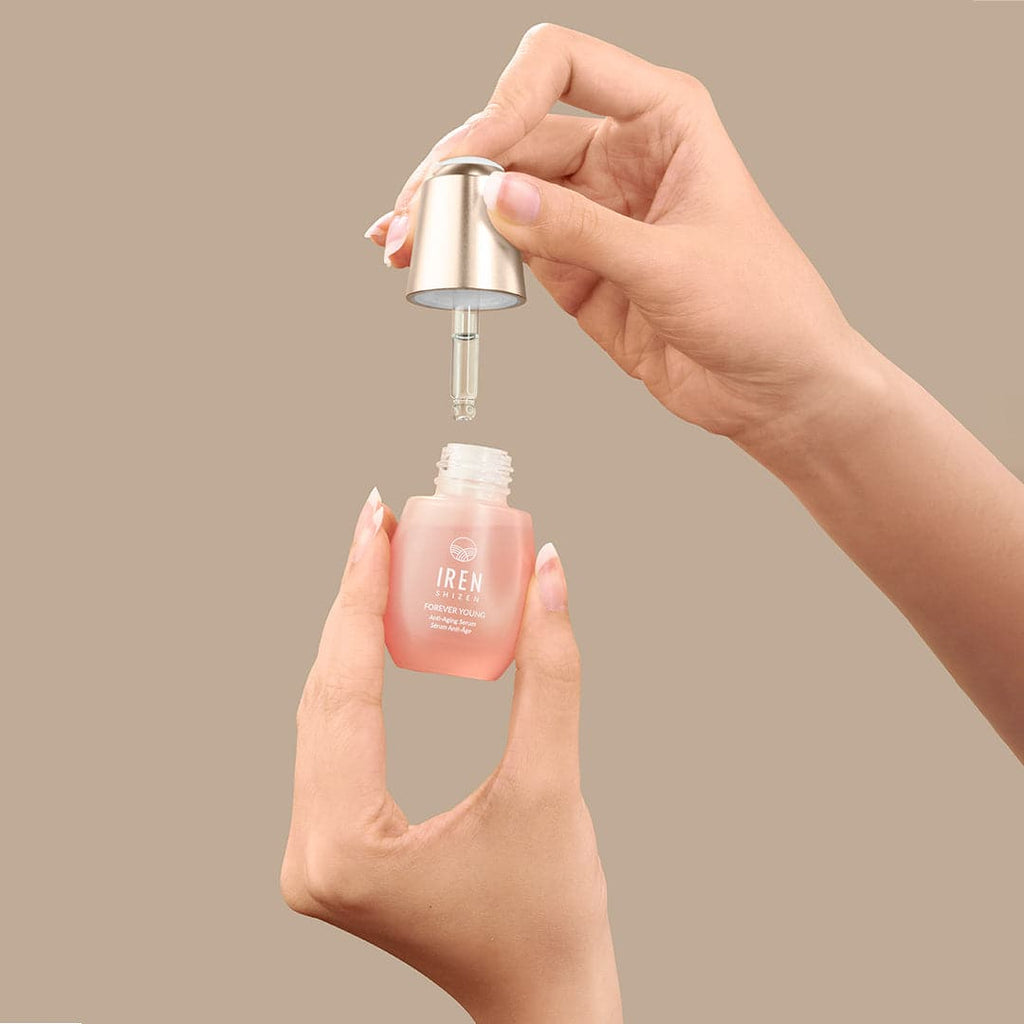 A hand is holding a bottle of custom ONSEN skincare FOREVER YOUNG Anti-Aging Serum by IREN Shizen on a beige background.