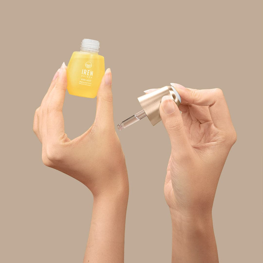 A woman's hands holding a small bottle of customized STAR LIGHT Brightening Serum by IREN Shizen, a Japanese skincare brand.