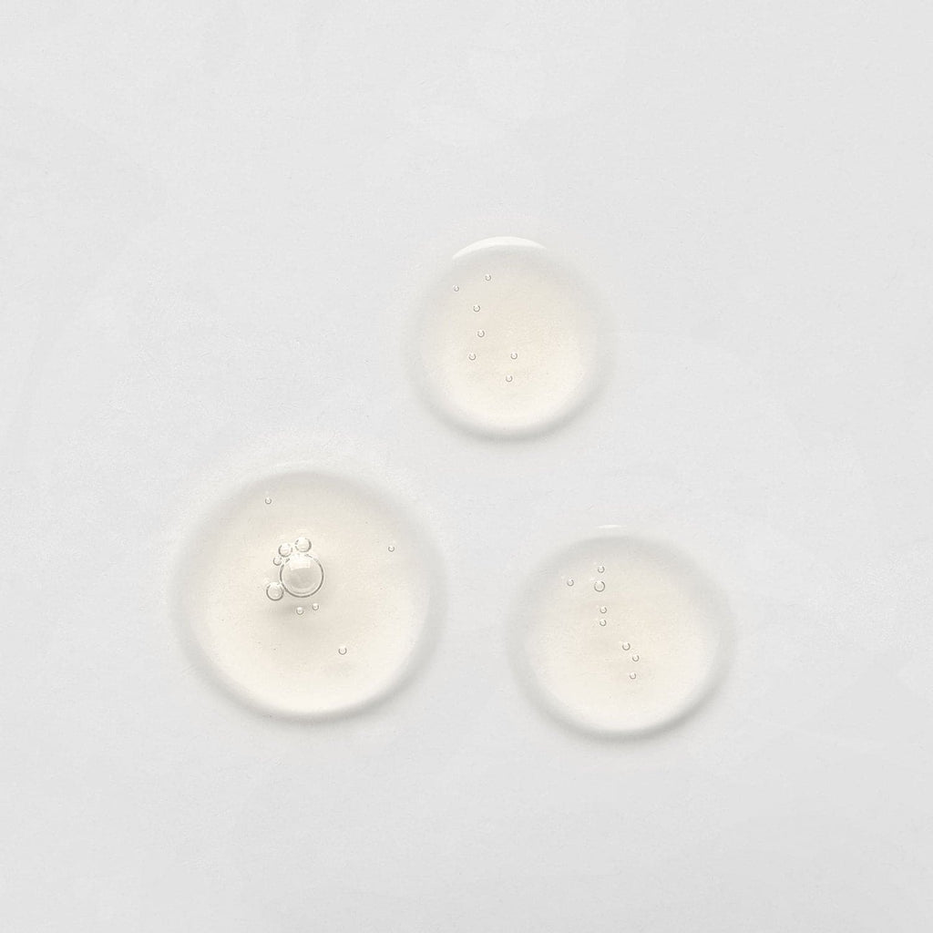 Three drops of IREN Shizen's custom Japanese skincare Anti-Aging Serum on a white surface.