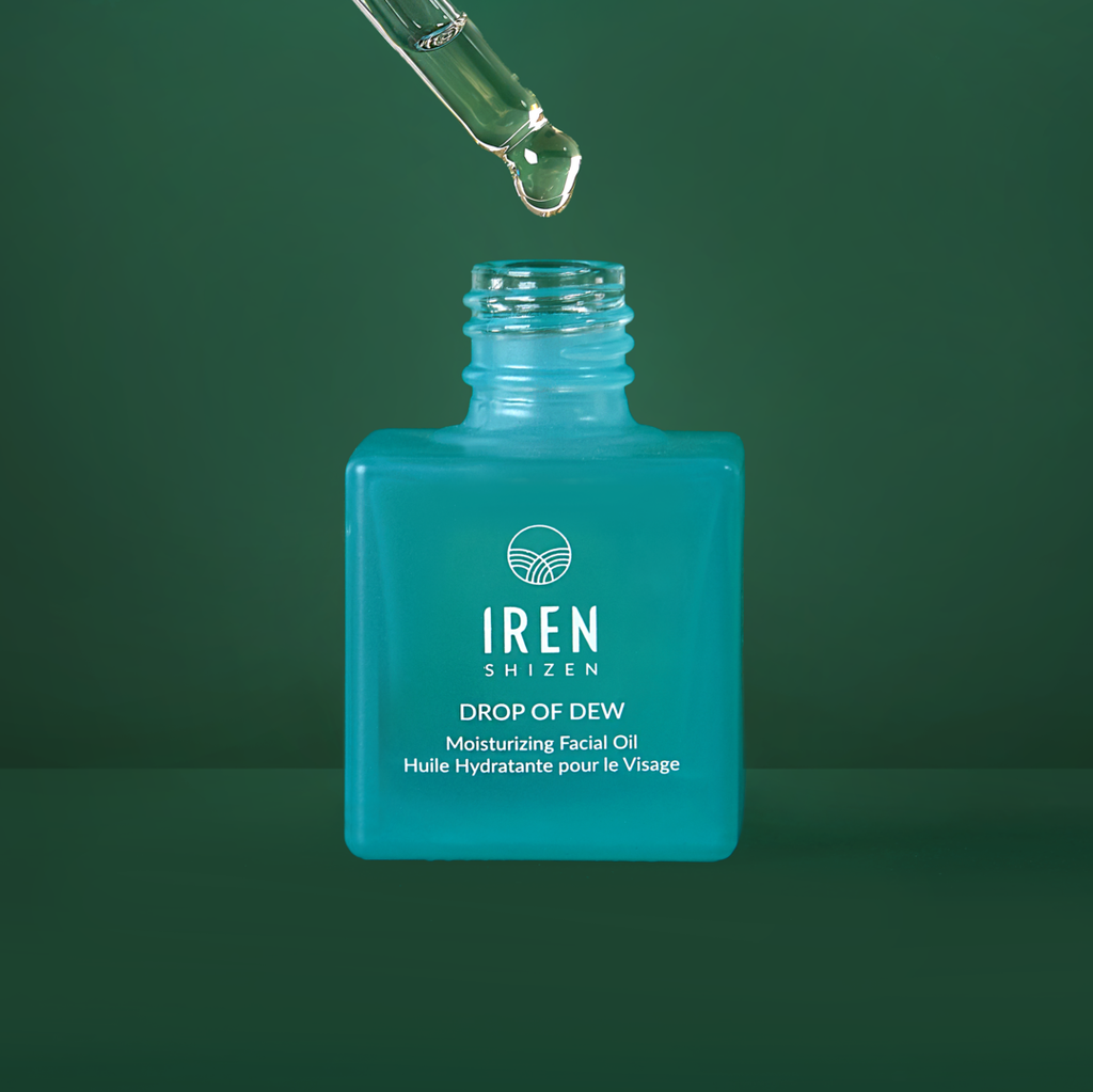 A bottle of customized DROP OF DEW Moisturizing Facial Oil by IREN Shizen on a green background.
