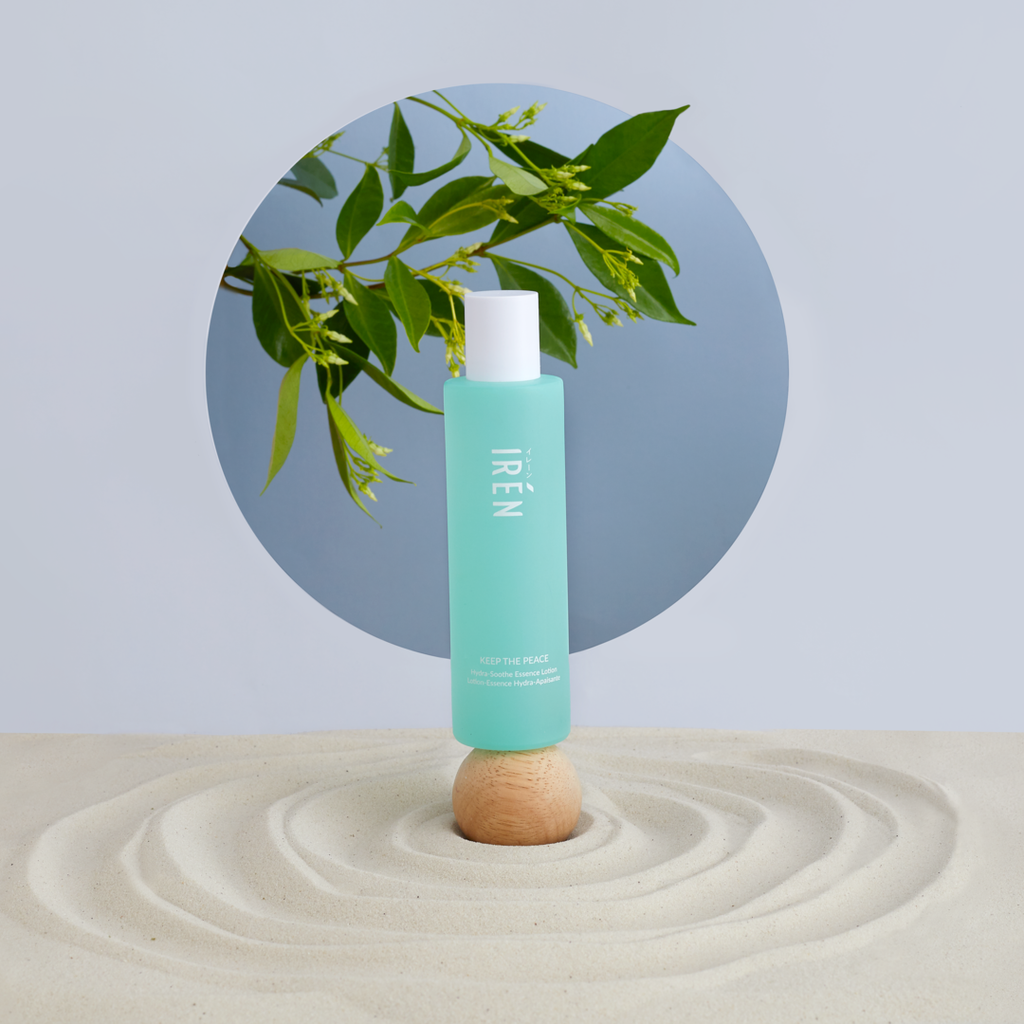 A bottle of KEEP THE PEACE Hydra-Soothe Essence Lotion by IREN Shizen sitting on top of a sand.